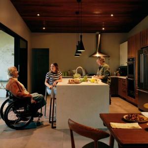 A person in a wheelchair talking with two others at a kitchen island.