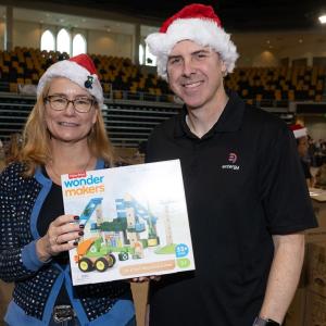 Two volunteers in santa hats posed together with a toy.