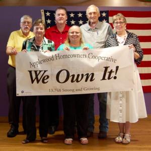 Applewood Homeowners Cooperative group shown in front of an American Flag and holding a sign that says "We Own It".