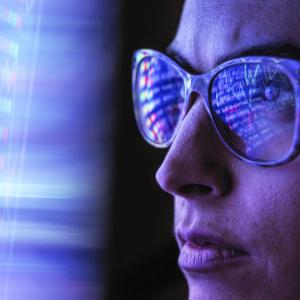 Person in front of blue digital light with reflection on their glasses