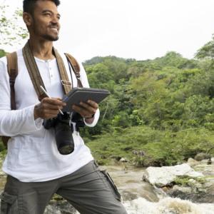 A smiling person with a camera and notepad next to a stream