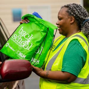 Volunteer handing bags of school supplies to community member in car