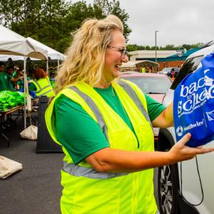 Volunteer handing backpack of school supplies to community member in car