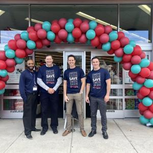 Four people posed outside a Walgreens. A balloon arch over the entrance.