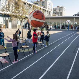 Children outside throwing basketballs against a wall.