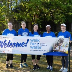 Five participants standing in front of Walk for Water banner