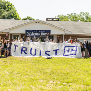 a large group of people outside the new home, a large "Truist" banner being held up