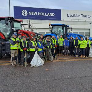 Volunteers standing together with trees to plant, in front of tractors at the Basildon Tractor Plant