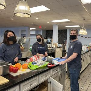 Four Bath & Body associates stand at long counter in the Ronald McDonald House preparing fresh vegetables.