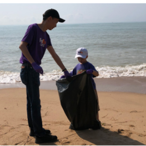 An adult and child holding a plastic bag on a beach.
