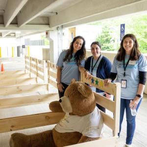 Three volunteers standing with a row of bed frames.