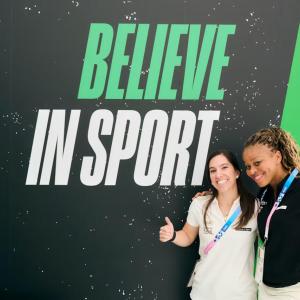 two people posing in front of "Believe in sport" banner
