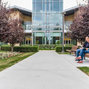 Two people sitting on a bench outside a building in a park like setting.