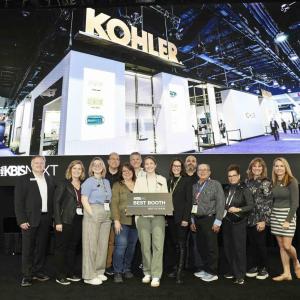 A team of people standing posed in front of the Kohler booth. One holds a sign "Best booth"