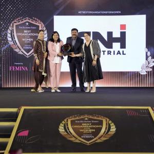 Four people on a stage, two holding an award. Large CNH banner behind them.