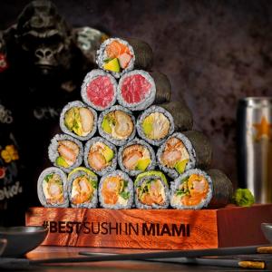 A pyramid of sushi rolls in a tray, beverages behind them.