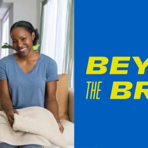 An adult and child sitting next to each other on a couch. One folding laundry and the other holding a bottle of detergent.