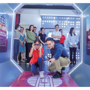 An adult and child crouched in an octagonal room with displays on each side. Others standing and waiting behind them.