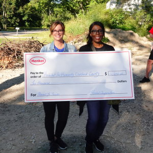 two people holding a large check made to Habitat for Humanity. Crew of volunteers behind them.