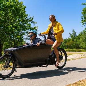 An adult operating a bicycle with large compartment in front with a child sitting inside.