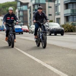 Pete Bowker and Daniel Usher riding e-bikes on a road.