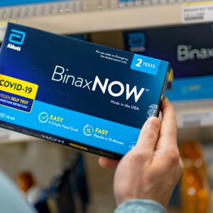 A person holding a BinaxNow Covid-19 test kit. 