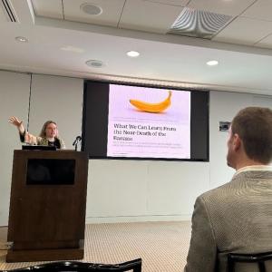 A presenter at a podium, a display behind them.