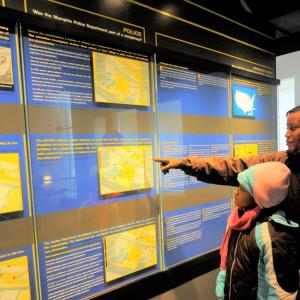 An adult pointing at a display in a museum setting. A child in front of them.
