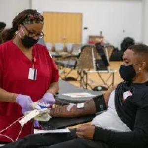 a person reclined donating blood, a healthcare worker by their side