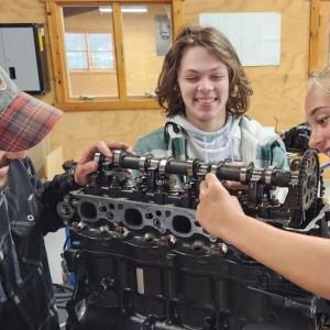 Three smiling people working on a large mechanical piece.