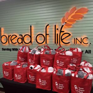 "bread of life" sign on a wall behind a table of filled red bags.