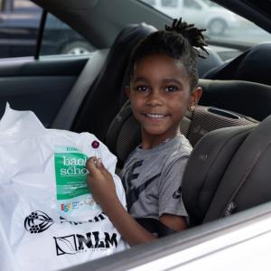 Student sitting in car holding a bag of school supplies