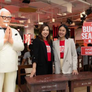 Two people in matching shirts standing behind a desk, next to a large statue of a person.