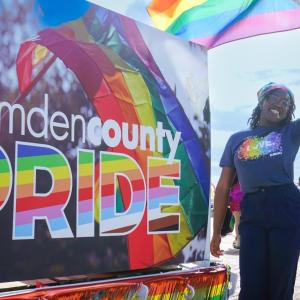 A person waving a pride flag next to a sign that says "Camden County PRIDE"
