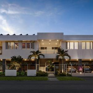 A photo of a building from the front with the lights turned on and large trees either side of the door