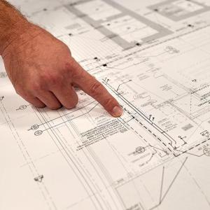 A person pointing to a spot on a building plan.