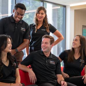 Five people posed casually inside. Some seated on a couch, some behind them.