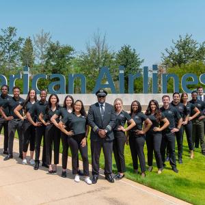 Group posed outside in a "V" formation. American Airlines sign behind them.
