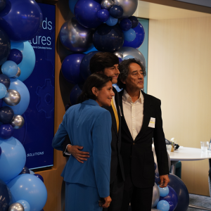 Three people posing for a camera beneath blue balloons
