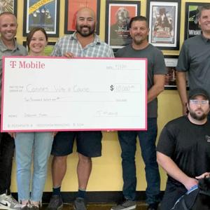 A small group posed with a large check in front of a wall of pictures.