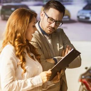 Two people in a car dealership looking at a clipboard.