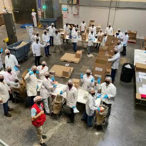 Aerial view of volunteers in protective coverings, working with boxes and food in a warehouse setting.