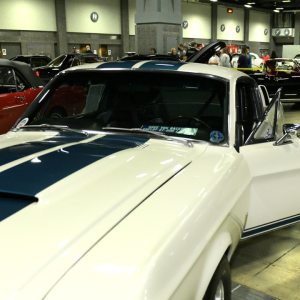 A person standing in the open door of a car at an auto show.