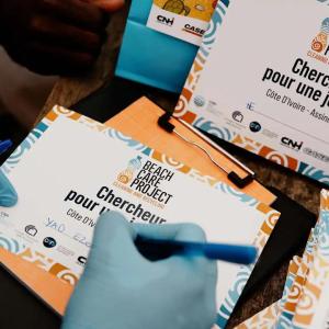 Person wearing blue gloves writing on a 'Beach Care Project' card