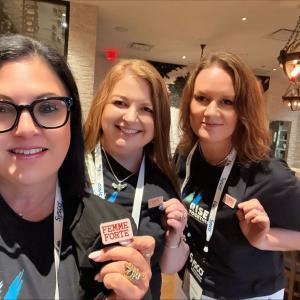 Three people holding up their "Femme Forte" buttons