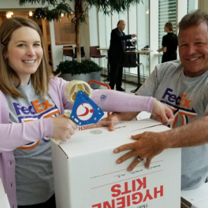 Two smiling people taping up a box that says "hygiene kits"