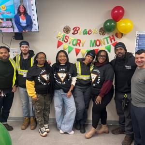 Eight people standing together in front of a banner: "Black History Month"