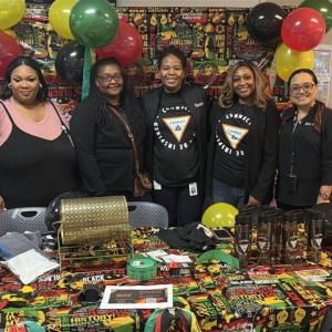 Five people standing together behind a table at an event, with balloons behind them