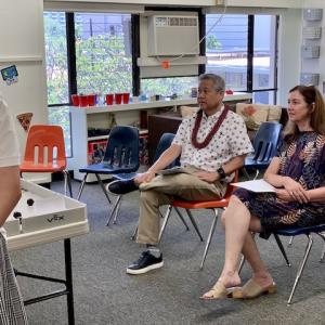 Two adults sitting in school chairs taking notes on presentations.