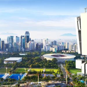 Elevated view of the top of a cell tower with a city skyline and urban area behind it.